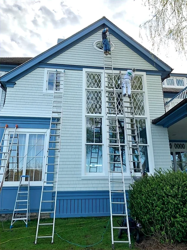 A man on a ladder painting the outside of a house